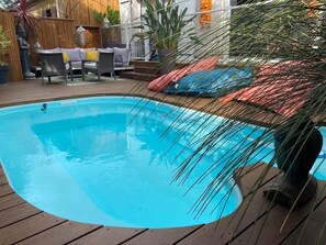 Une piscine dotée d’une terrasse en bois, entourée de meubles d’extérieur et de plantes.