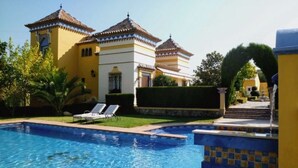 En swimmingpool med solstolar, en välskött gräsmatta och en byggnad med traditionell arkitektur.