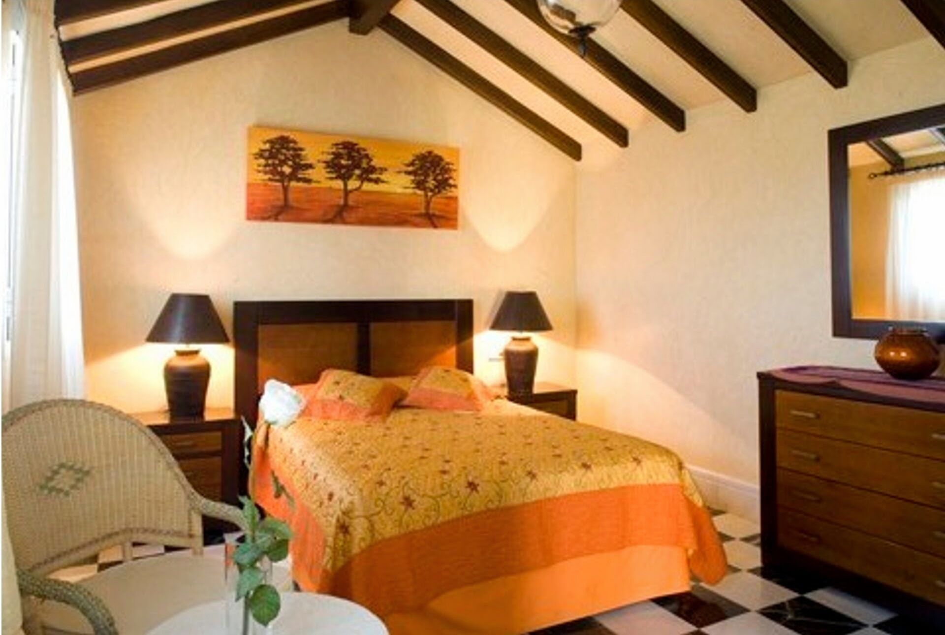 Un dormitorio con una cama, dos lámparas de noche, una silla, un aparador y un cuadro de árboles en la pared.
