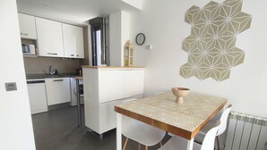 Eine kompakte Küche mit weißen Schränken, einer Mikrowelle und einem Spülbecken. Es gibt einen Essbereich mit Tisch und Stühlen sowie ein dekoratives Wandbild.