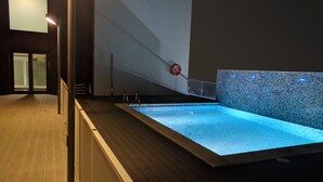 Ein moderner, überdachter Schwimmbereich mit klarem Wasser, Holzboden und Fliesenwand.