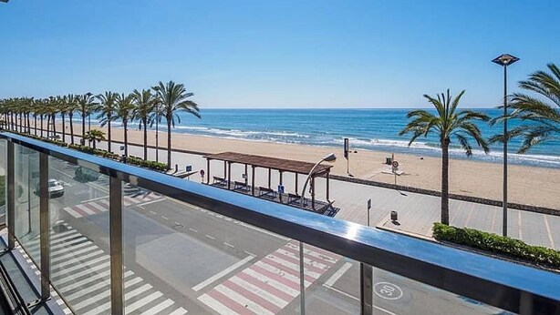Ein Balkon mit Blick auf einen Strand, Palmen und einen klaren, blauen Himmel.