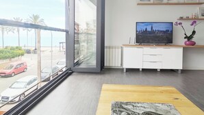 Ein modernes Wohnzimmer mit großem Fenster, einem Flachbildfernseher, einem Holztisch und einer weißen Kommode.