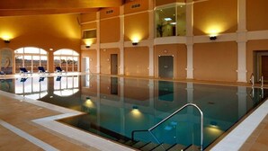 Ein Hallenbad mit großen Glaswänden, mehreren Liegestühlen und einem gefliesten Boden.