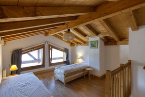 A room with a wooden ceiling, a bed, a small table, and a window with curtains.