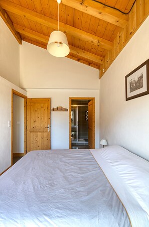 A bedroom with a wooden ceiling, a bed with white bedding, a hanging lamp, a door, and a framed picture on the wall.