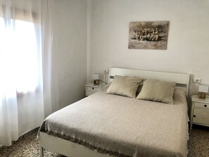 Une chambre à coucher comprenant un lit, deux tables de chevet, une œuvre d’art accrochée au mur et une fenêtre avec des rideaux.