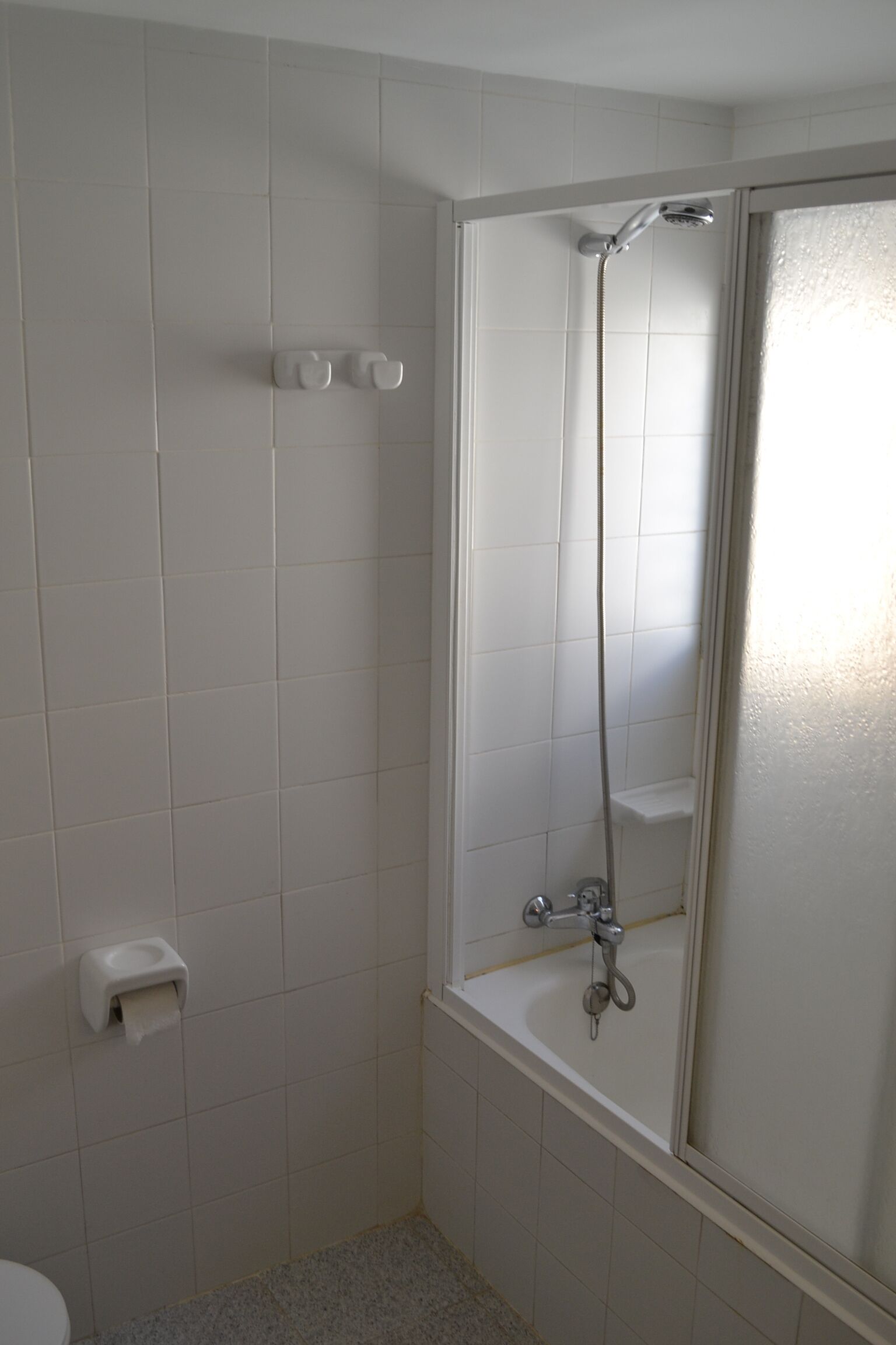 A bathroom with white tiles, a toilet, a shower with a glass door, and a soap dispenser.