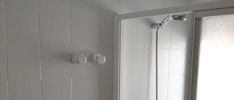 A bathroom with white tiles, a toilet, a shower with a glass door, and a soap dispenser.