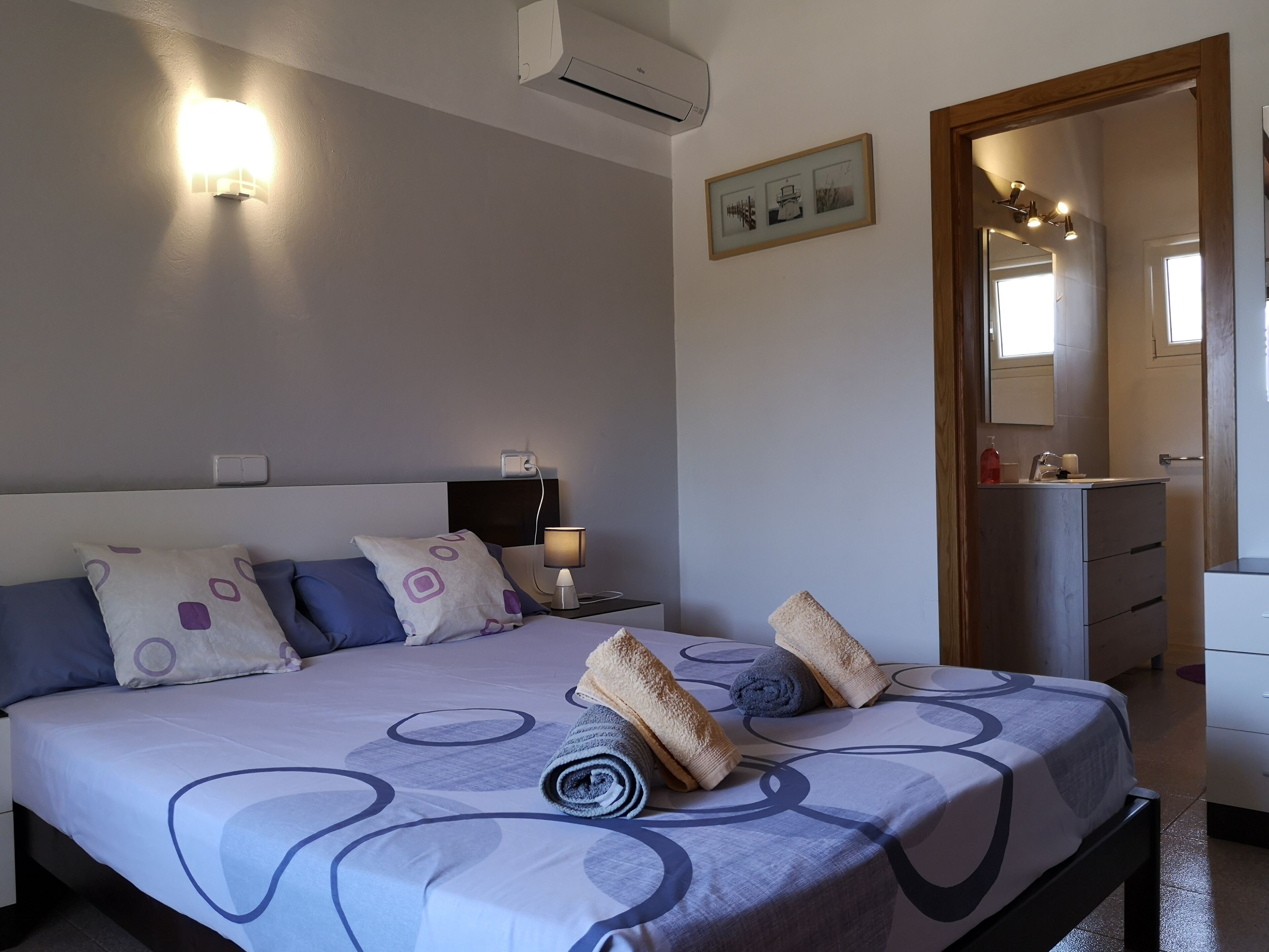 A bedroom with a bed, bedside table, lamp, and a mirror.