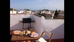 Eine Dachterrasse mit Tisch für Zwei, einem Grill und Blick auf die Stadtlandschaft.