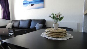 Ein Wohnzimmer mit einer schwarzen Ledersofa, einem Esstisch mit gewebter Tischmatte und einem Blumentopf, sowie einem Laptop auf dem Sofa.