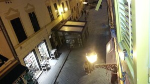 Una calle estrecha flanqueada por edificios, una tienda con exhibición de frutas y una persona caminando.