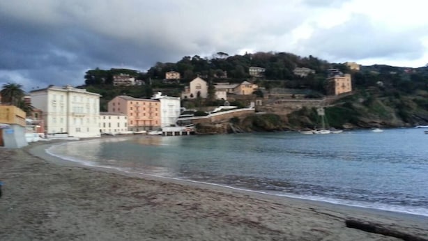 Un pueblo costero con edificios a lo largo de la playa y una colina con casas al fondo.