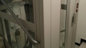 Una escalera con puerta de ascensor de vidrio, barandillas de metal y suelo de baldosas.