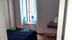Una habitación pequeña y poco amueblada con cama, radiador y ventana con cortinas.