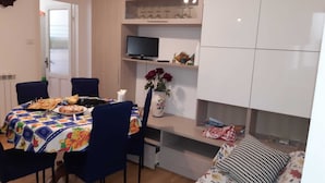 Un comedor con una mesa lista para cuatro personas, un televisor en una estantería y una cama con ropa de cama floral.
