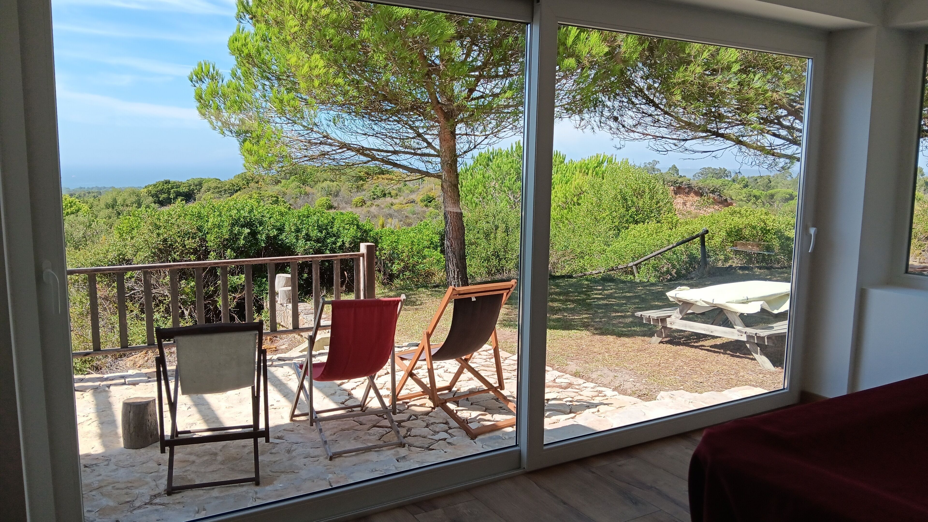 A room with a large sliding glass door leading to an outdoor area with a wooden deck, two chairs, and a table.