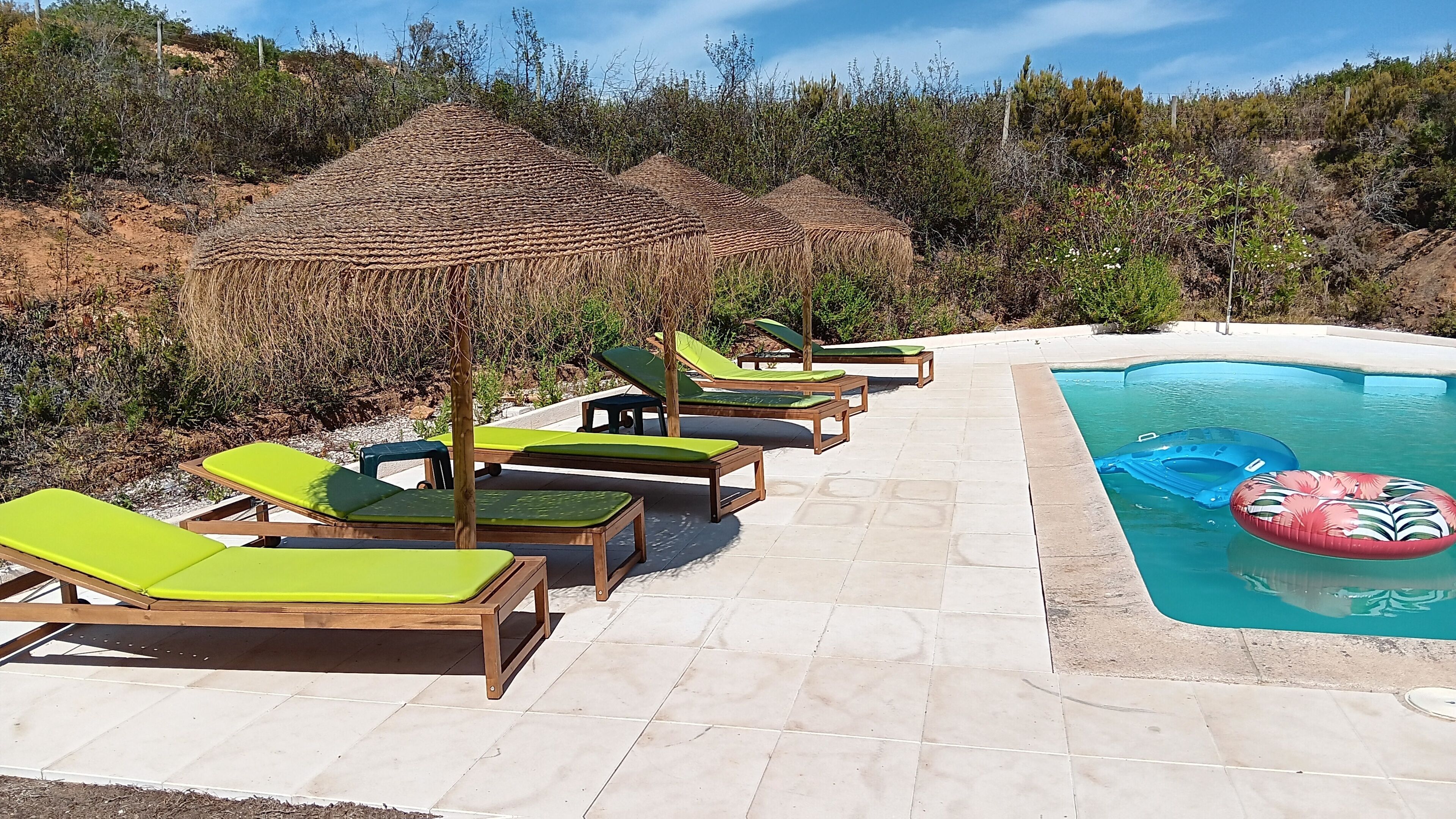 A poolside area with lounge chairs and a thatched structure.