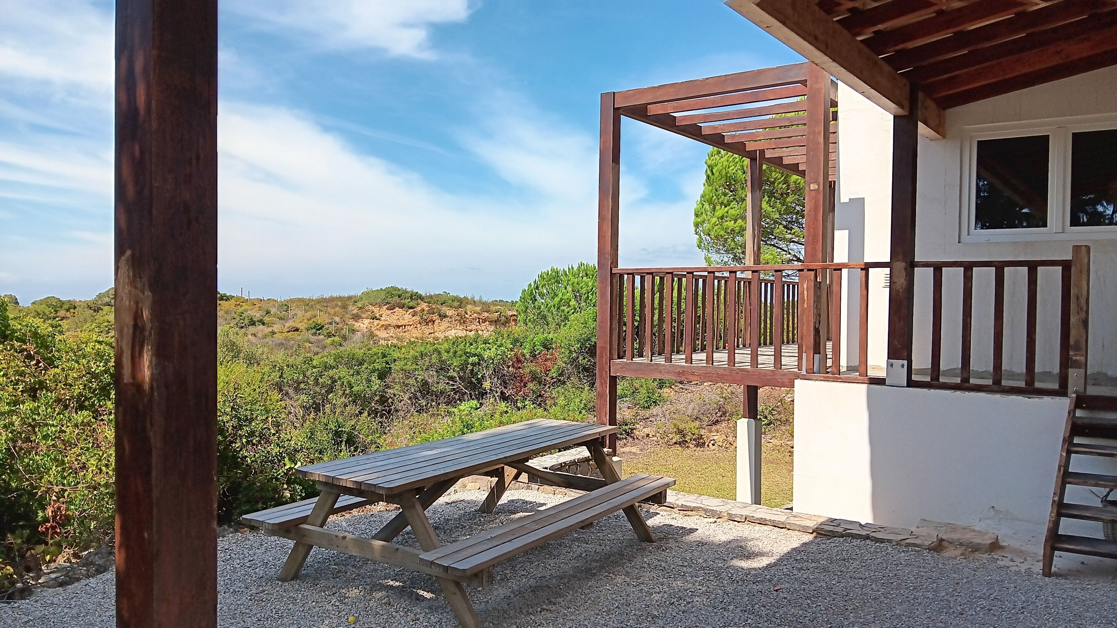 A wooden deck with a picnic table, a wooden pergola, and a view of a vineyard.