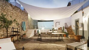 Une terrasse extérieure rustique, avec un mur en pierre, une table en bois et une chaise suspendue.