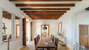Un vaste espace dédié à la salle à manger, avec une longue table en bois entourée de chaises, le tout sous des poutres apparentes.