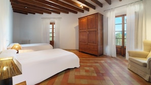 Une chambre avec deux lits, des poutres en bois au plafond, une grande armoire et une vue par la fenêtre.
