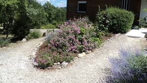A wooden house with a red-tiled roof, surrounded by gravel and flowering bushes. - Timber frame house with garden (Vers)