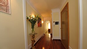 Ein Flur mit Holzboden, einer Glasvase mit Blumen, einem gerahmten Bild an der Wand und einer Tür am Ende.