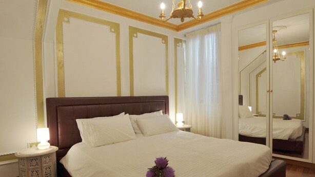 Ein großes Bett mit hölzernem Kopfteil, ein Nachttisch mit Lampe und ein Spiegel an der Wand.