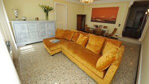 Ein Wohnzimmer mit Ecksofa, einem weißen Schrank, einem Esstisch mit Stühlen und einer Deckenleuchte.
