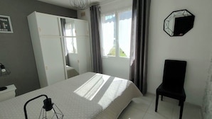 A bedroom with a bed, a wardrobe, a chair, and a window with curtains. - T2, 350 m from Bodri BEACH, Sea view, Air-conditioning, on large landscaped grounds. (Corbara)