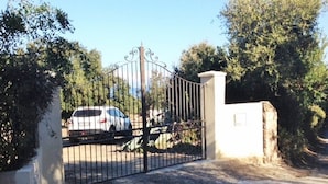 A gated driveway with a parked car and a stone pillar. - T2, 350 m from Bodri BEACH, Sea view, Air-conditioning, on large landscaped grounds. (Corbara)