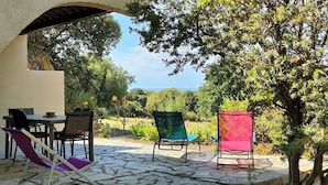 An outdoor patio with a table and chairs, surrounded by lush greenery and a clear sky. - T2, 350 m from Bodri BEACH, Sea view, Air-conditioning, on large landscaped grounds. (Corbara)