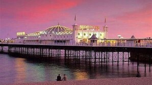 En strandpromenad med en brygga och en byggnad som är märkt med texten ”Brighton Pier”.