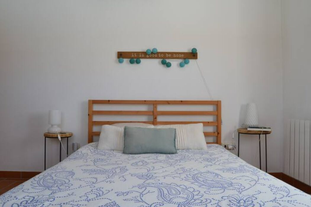 A bedroom with a wooden headboard, a patterned bedspread, a pillow, a wall-mounted decoration, and bedside tables with lamps.