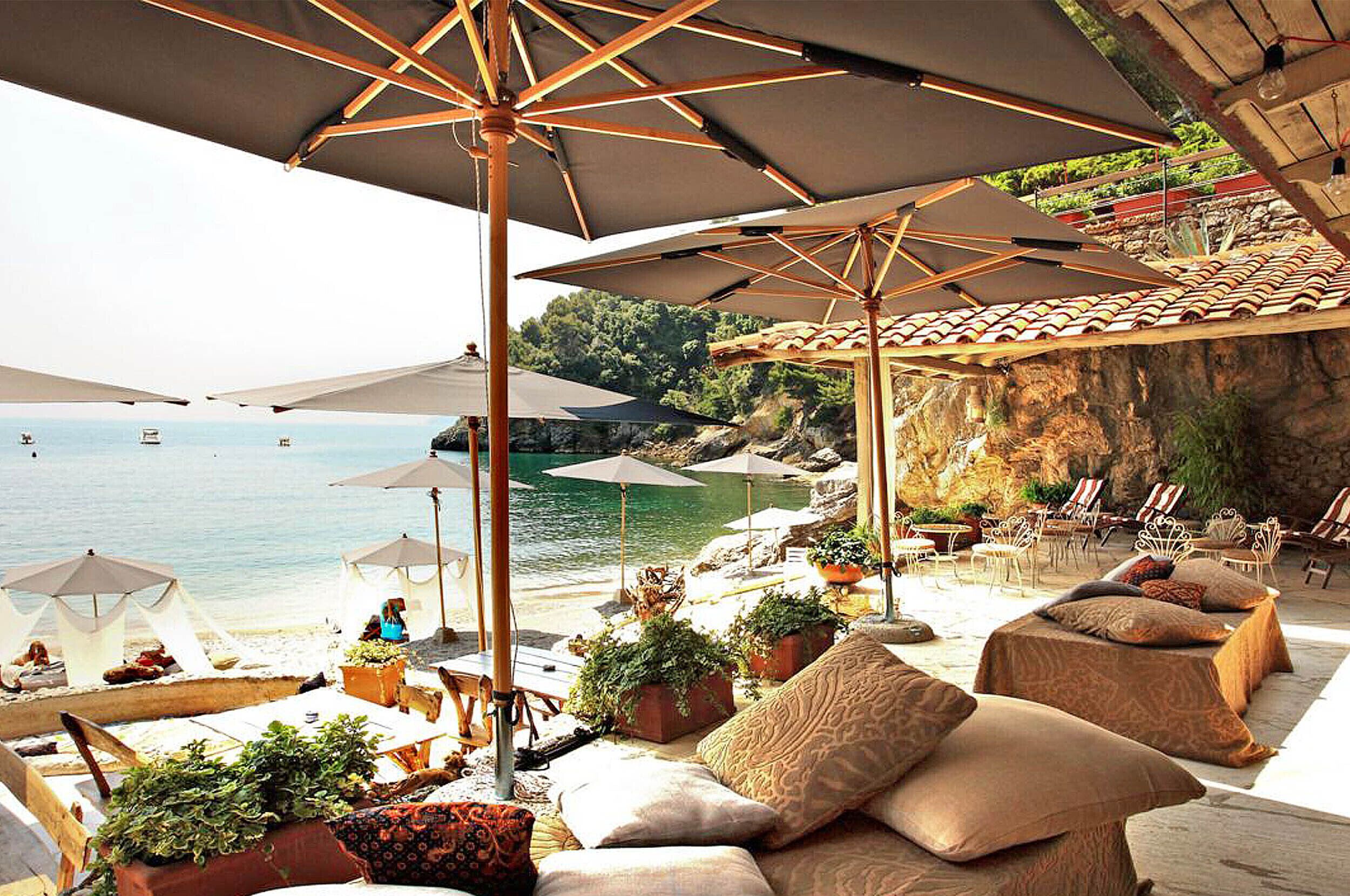 Un salon de plage avec des espaces de détente en plein air, des parasols et des plantes en pot.