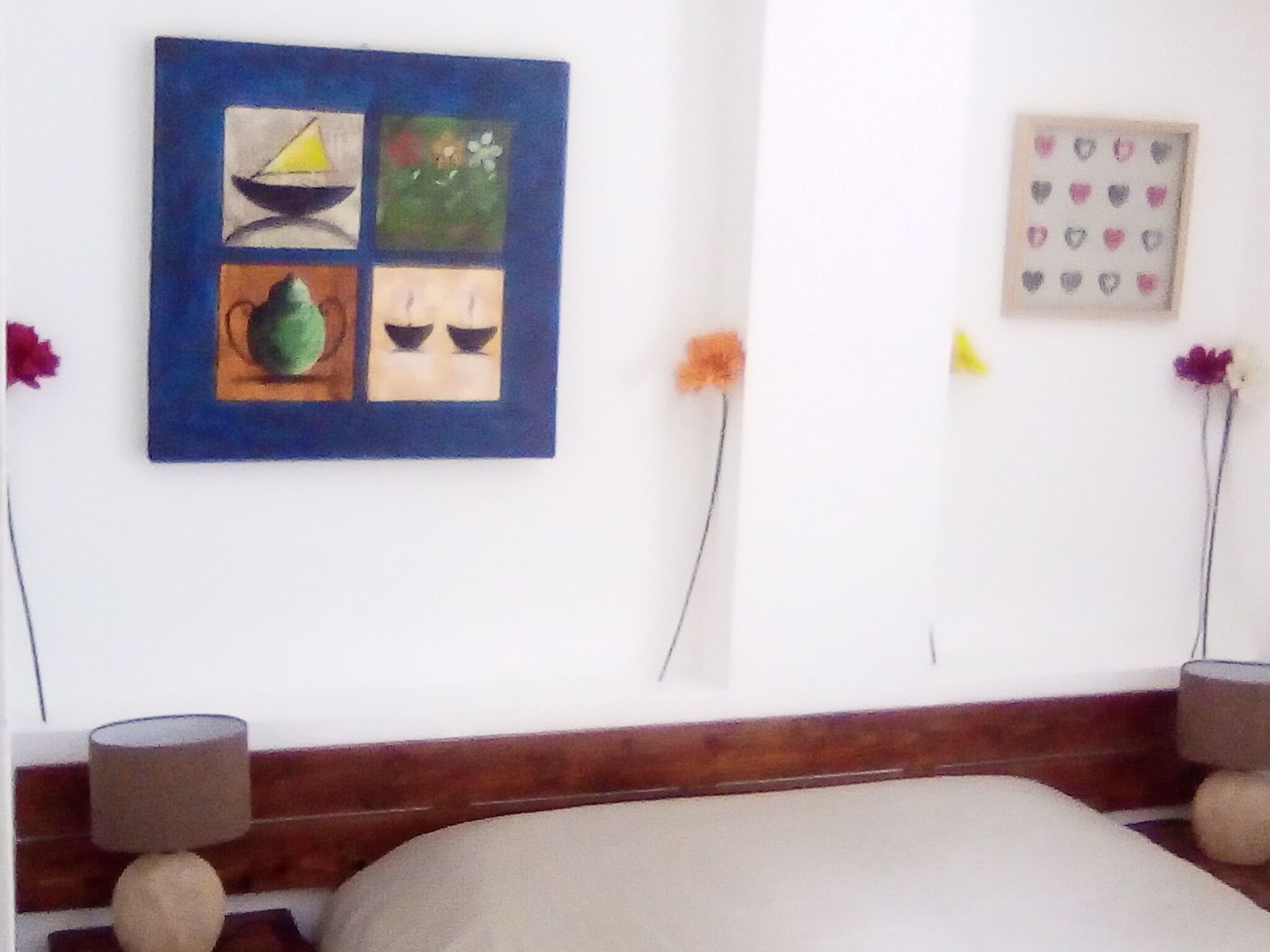 A bedroom with a bed, a wall-mounted artwork, and a small potted plant.