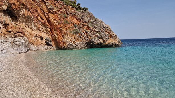 Una costa rocosa con agua turquesa cristalina y una playa de guijarros.