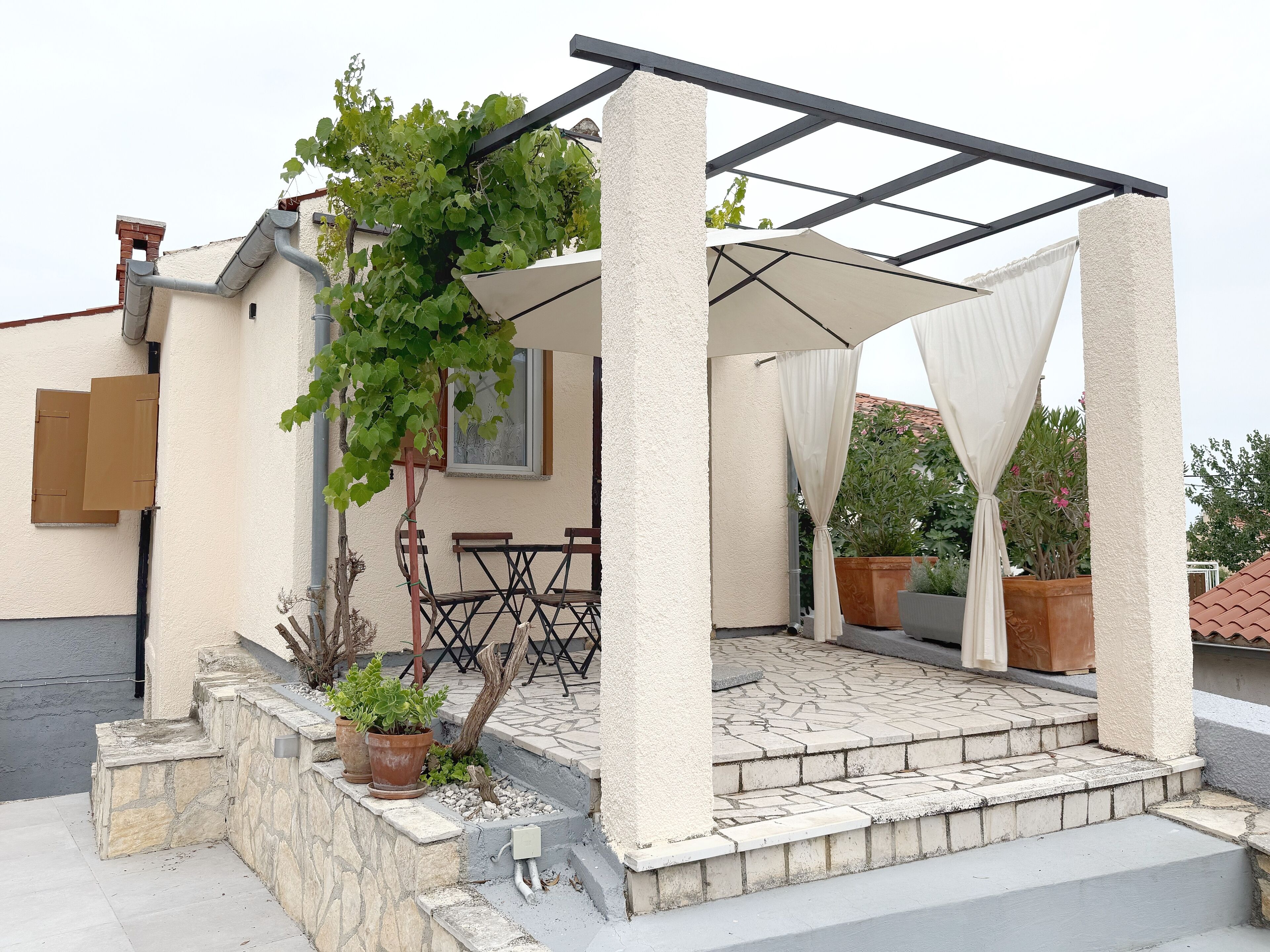 A covered outdoor seating area with a pergola, stone steps, and potted plants.
