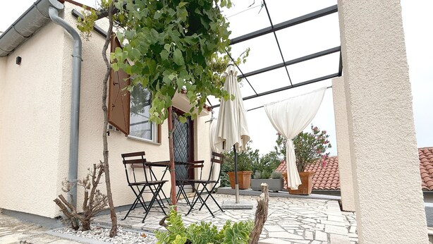 A patio area with a stone wall, two potted plants, a wooden table and chairs, and a pergola with vines. - LacoDeLama mini resort apartment Pina (LIZNJAN)