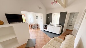 A modern living room with a sofa, a small table, and a TV on the wall. There is a kitchen area with a dining table and chairs, and a bathroom with a shower. - LacoDeLama mini resort apartment Pina (LIZNJAN)