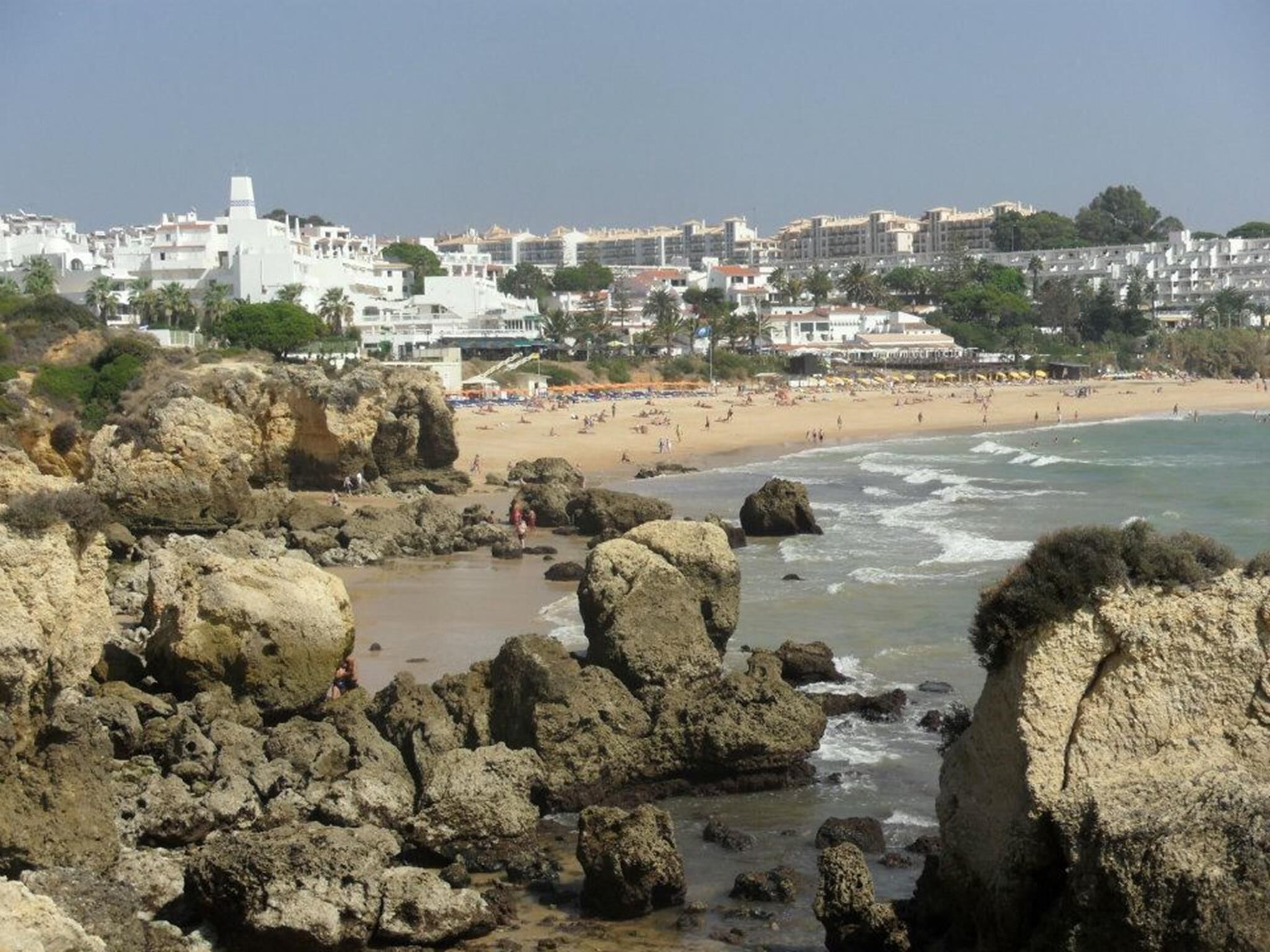 Un poble costaner amb vores rocoses, una platja de sorra i edificis al fons.