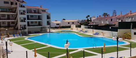 A swimming pool with a geometric design, surrounded by a fence and sun loungers.