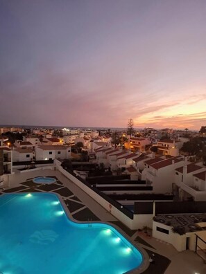 A swimming pool with a view of a coastal town at dusk.