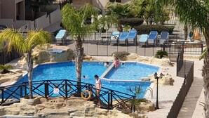 Ein Pool mit Felsgestalt, umgeben von Liegestühlen und Palmen.