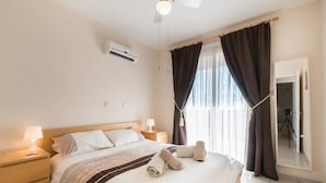 Ein Hotelzimmer mit einem Bett, Nachttischlampen, einem Deckenventilator, einer Klimaanlage und einem Fenster mit Vorhängen.