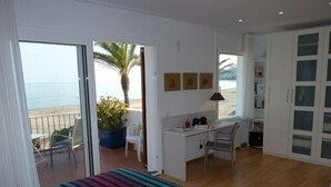 Une chambre avec un lit, un bureau et une chaise. Elle possède un balcon avec vue sur la plage et les palmiers.