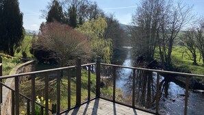 Une terrasse en bois avec une balustrade donnant sur une rivière et un mur en pierre.