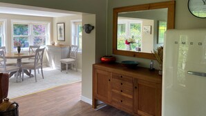 Une cuisine spacieuse avec une table à manger en bois, des chaises blanches, un grand miroir et un réfrigérateur moderne.